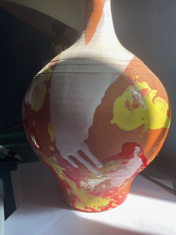 A terracotta vase with red, yellow and white drips